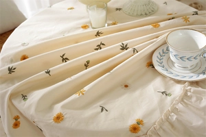 Close-up of apricot cotton tablecloth with embroidered daisies and ruffled edges