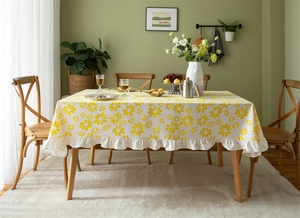 Detailed view of yellow daisy floral patterns and ruffle edges on a cotton tablecloth