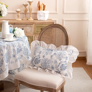 French country floral lumbar pillow with white ruffled edges on a vintage wicker chair