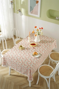 Detail of white pom-pom trim on rectangular cotton tablecloth with pink floral print