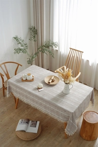 Close-up of beige rectangular tablecloth with white geometric embroidery and tassel fringe
