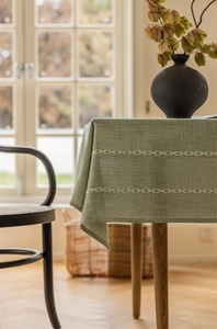 Detail of sage green jacquard tablecloth featuring white cross-stitch embroidery and texture