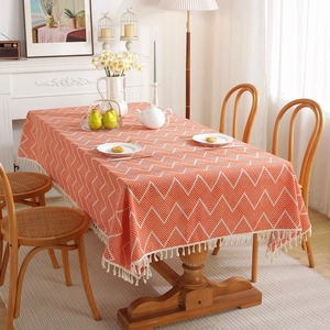 Bohemian orange and white herringbone tablecloth with fringe tassels on a wooden dining table