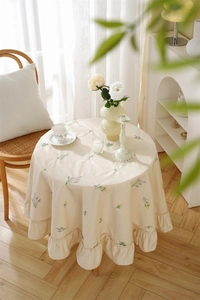 Macro detail of lavender floral embroidery and ruffled edge on beige round cotton tablecloth