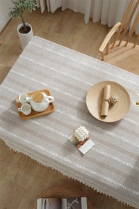 Close-up of beige jacquard tablecloth with white embroidered stripes and fringe edges
