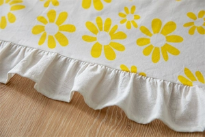 Detail of yellow daisy floral print on white cotton fabric with elegant ruffled edges