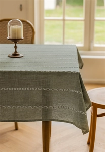 Detailed view of green cotton linen tablecloth with elegant white embroidered pattern