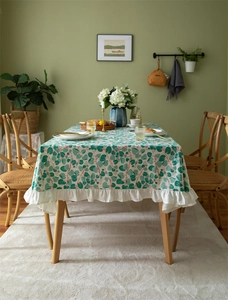 Close-up of floral cotton tablecloth featuring green leaves and white ruffled edges