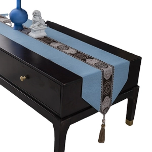 Light blue Chinese table runner with traditional embroidery and brown tassels on wood desk