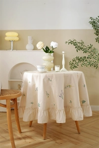 Detail of cream cotton tablecloth featuring floral embroidery and ruffled edge design