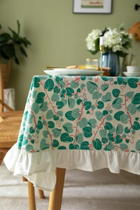 Detail of floral printed tablecloth with elegant white ruffled edges and green leaves