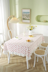 Detail of white cotton tablecloth featuring red strawberry prints and ruffled edges