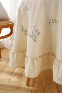 Detail of cream cotton tablecloth featuring floral embroidery and elegant ruffled hem edges