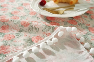 Close-up of cotton floral tablecloth with pink rose patterns and white pom-pom edges