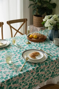Detail of floral printed cotton tablecloth with green leaves and white ruffled edges