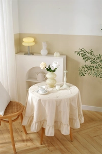 Detailed view of beige cotton tablecloth featuring floral embroidery and ruffled edge design