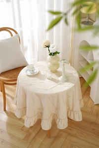 Detail of elegant beige cotton tablecloth with floral embroidery and ruffle edges