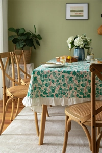 Detail of floral cotton tablecloth featuring green leaf prints and white ruffled edges