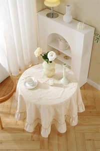 Detailed close-up of cream cotton round tablecloth with floral embroidery and ruffle edge