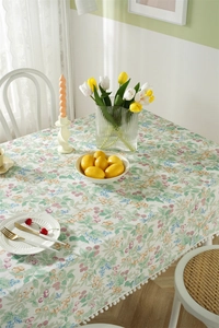 Detail of floral cotton tablecloth featuring white pom-pom fringe and spring botanical print