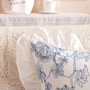 Close-up of French pastoral ruffled edges and blue floral embroidery on cotton pillowcase