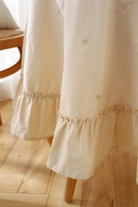 Close-up of beige cotton tablecloth featuring floral embroidery and ruffled hem edges