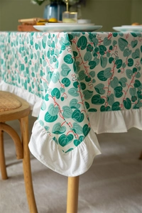 Detail of floral cotton tablecloth featuring green leaf patterns and elegant ruffled edges