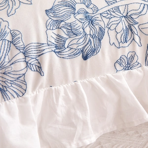 Detail of blue floral embroidery and ruffle edge on white cotton tablecloth fabric