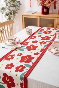 Detail van een crème tafelloper met rode bloemmotieven en keramisch serviesgoed