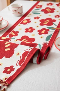 Detailopname van crème tafelloper met rode bloempatronen en elegante kwastjes