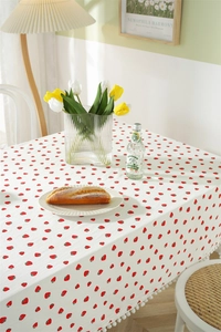 Detailed close-up of cotton tablecloth with red strawberry print and white pom-pom trim