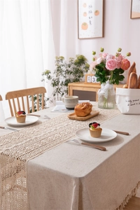 Close-up of beige linen tablecloth with dense fringe and vintage hollow lace table runner