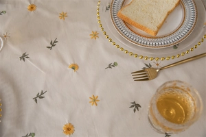 Close-up of apricot cotton tablecloth featuring daisy embroidery and ruffled edge detail