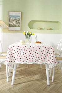 Close-up of strawberry print cotton tablecloth featuring decorative white pom pom fringe