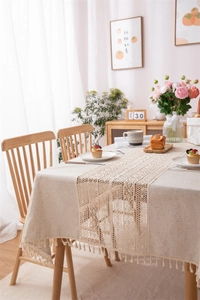 Detailed close-up of cream linen tablecloth with intricate lace stitching and fringe tassels