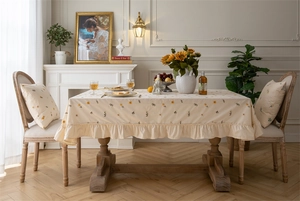 Detailed embroidery of daisies and elegant ruffle edge on beige cotton tablecloth