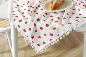Detailed close-up of white cotton tablecloth with strawberry print and white pom-pom trim edge