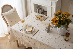 Close-up of beige cotton tablecloth with yellow daisy embroidery and ruffle hem edge