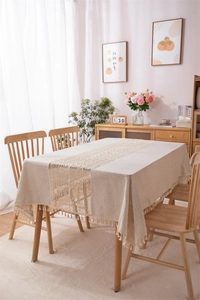 Close-up of beige linen tablecloth featuring intricate lace insert and cotton fringe tassels