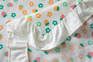 Detailed view of the strawberry flower print and ruffled lace edge on the cotton tablecloth