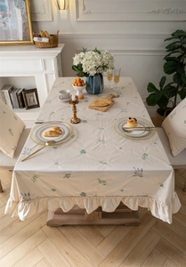 Detailed embroidery of yellow and purple flowers on beige cotton tablecloth with ruffles