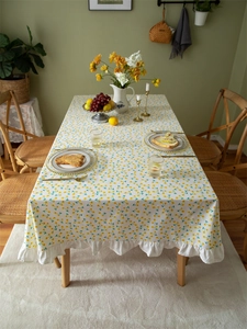 Detail of yellow daisy floral cotton tablecloth with white ruffled edges on wooden table