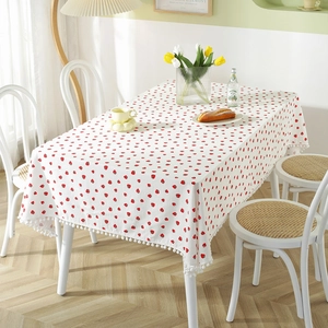 White cotton tablecloth with strawberry print and white pom-pom fringe in home setting