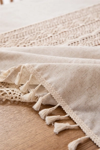 Detail of linen tablecloth with crochet lace edge and tassels on a wooden surface