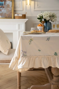 Close-up of ruffled edges and delicate floral embroidery on cream cotton tablecloth