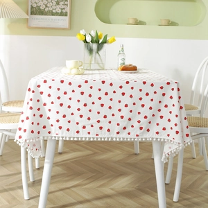 Fresh cotton strawberry print tablecloth with decorative pom pom fringe on a wooden table