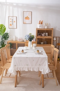 Detail of white cotton tablecloth with small floral embroidery and pleated ruffle edges