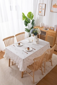 Close-up of cream rectangular cotton tablecloth with floral embroidery and ruffle edge