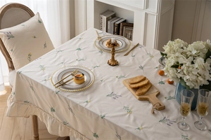 Detailed embroidery of lavender flowers on cream cotton tablecloth with ruffle edges