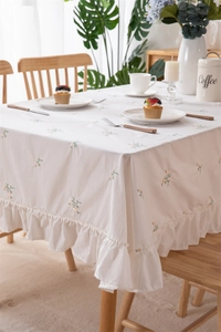 Close-up of floral embroidery and ruffled edge details on white cotton tablecloth